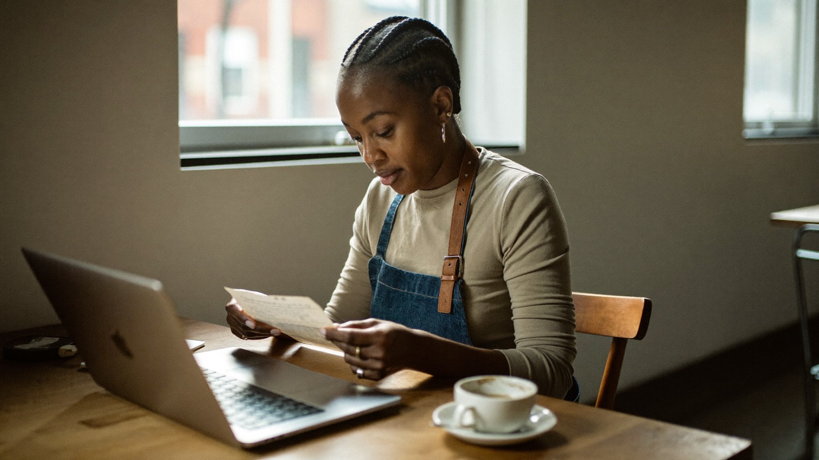 A café owner reviewing a marketing proposal on a laptop at a window table in her shop