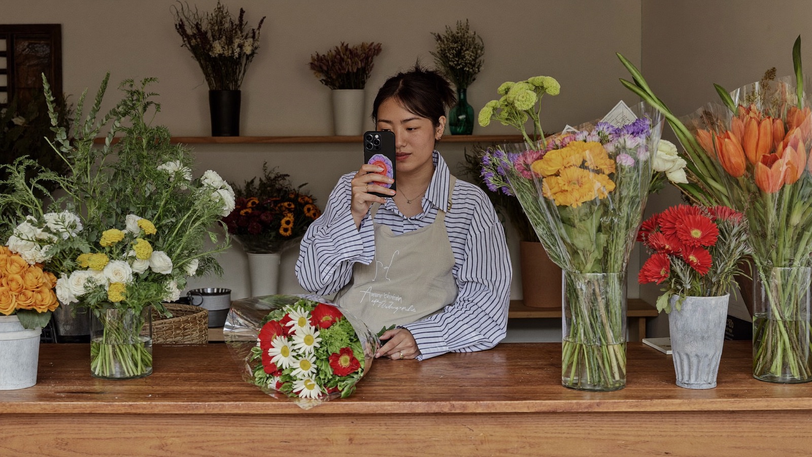 A florist photographing a bouquet with her phone on the counter of her shop